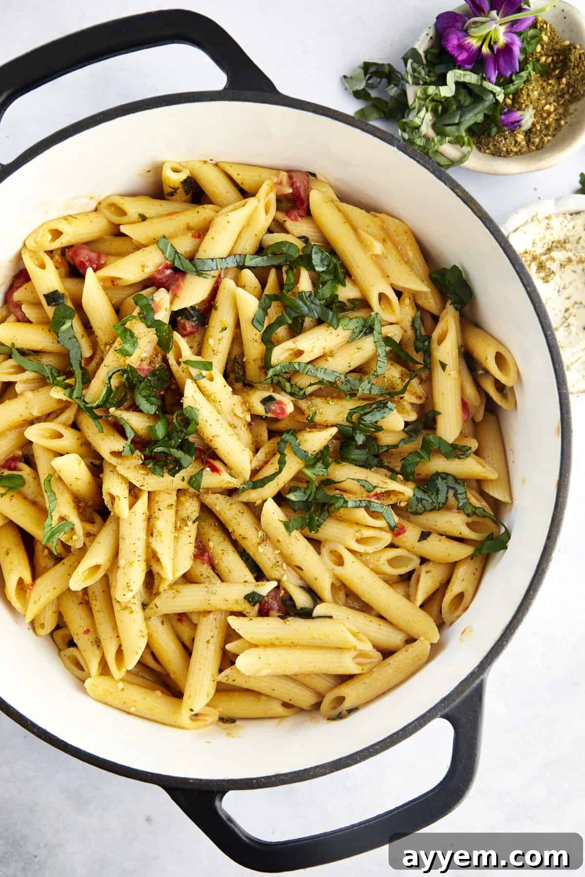An overhead shot of cooked penne pasta, vibrant pimento peppers, and fragrant seasonings expertly mixed in a single pot, showcasing the rich, creamy texture of the hummus pasta.