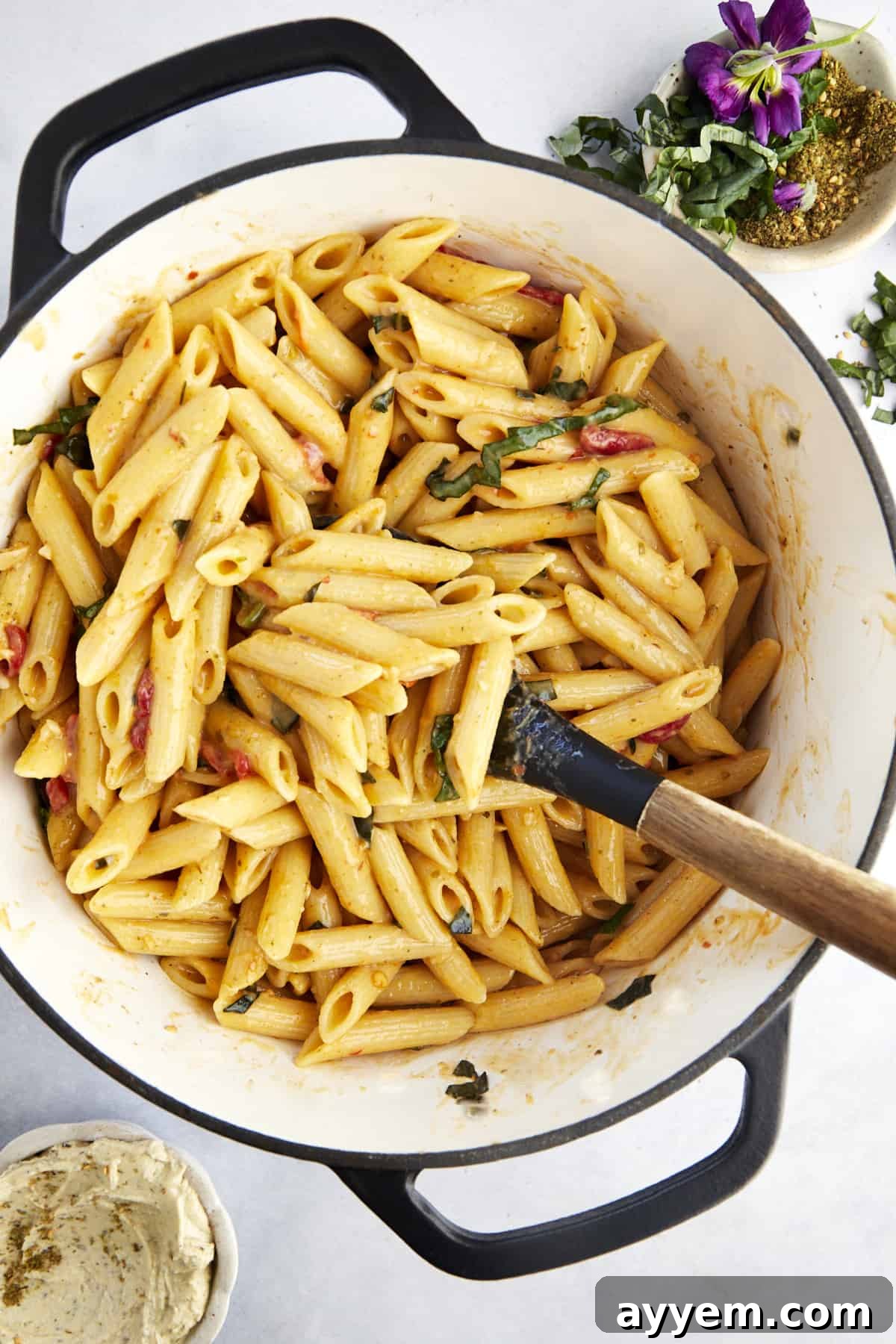 A rubber spatula gently stirs the luscious, creamy One Pot Hummus Pasta in a large cooking pot, revealing the tender noodles and perfectly integrated sauce.
