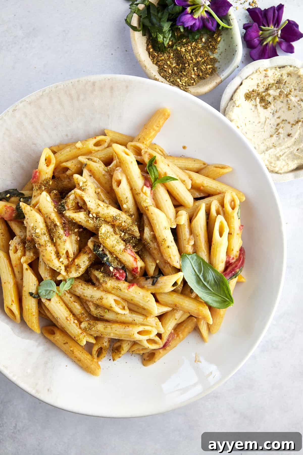 A vibrant plate of One Pot Hummus Pasta garnished with a delicate sprinkle of za'atar and fresh basil leaves, showcasing its rich texture and inviting appearance.
