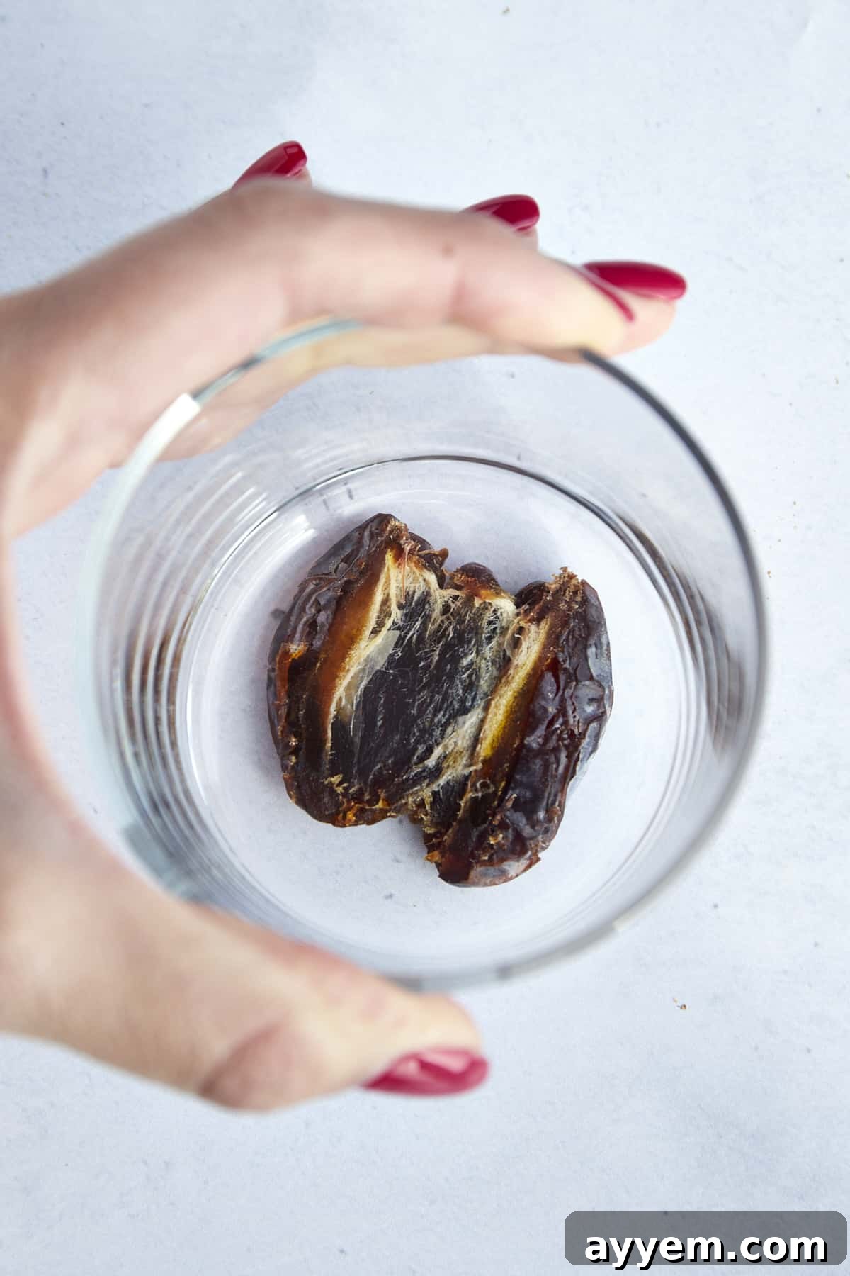 A hand using a cup to smash a date. 