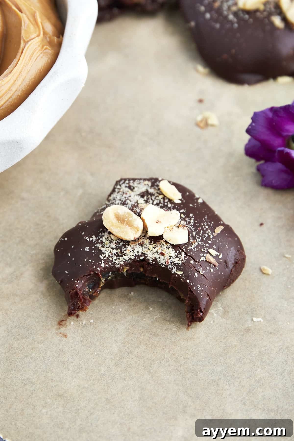 A chocolate covered date topped with peanuts with a bite missing. 