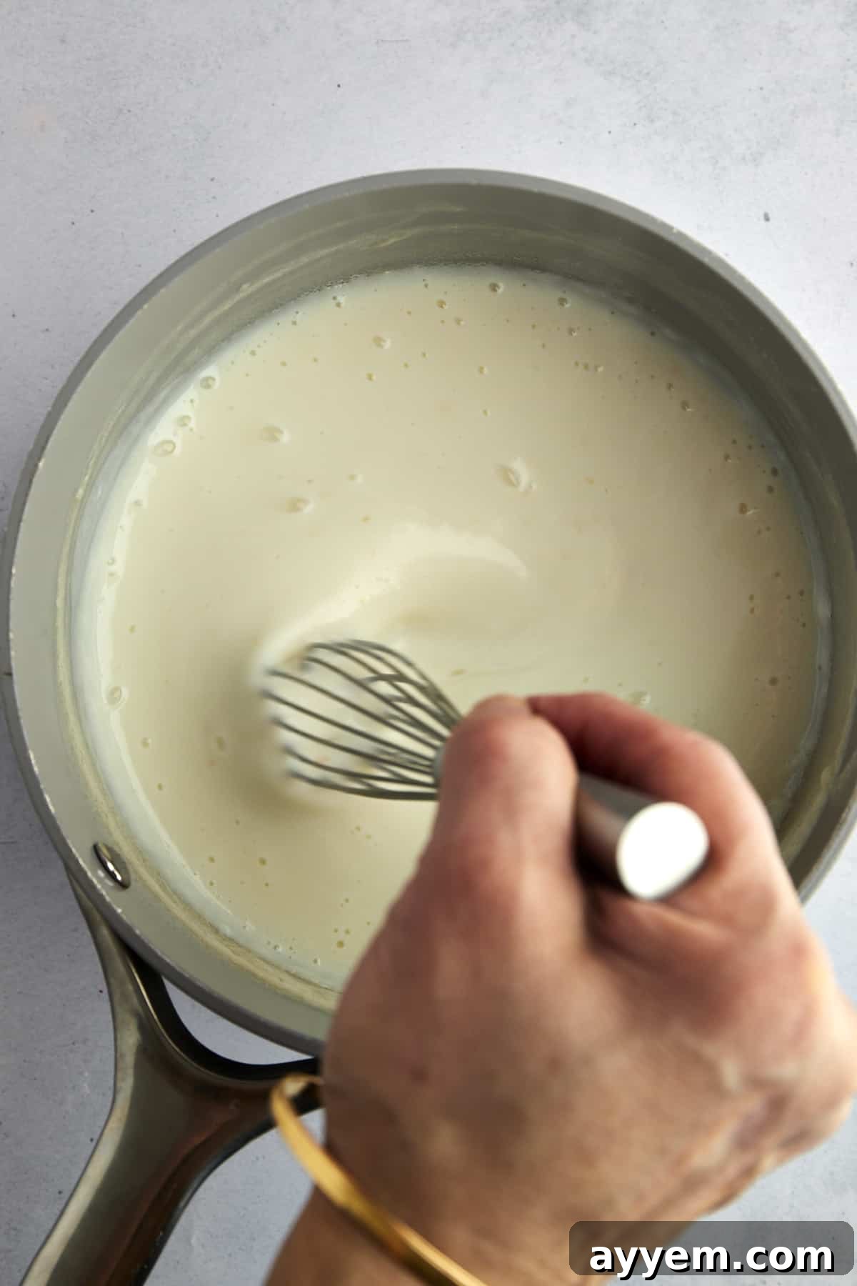 A hand whisking milk pudding to ensure a smooth consistency.
