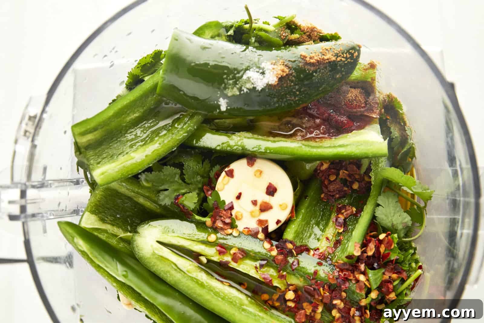 All the essential ingredients for Zhoug sauce, including fresh herbs, peppers, garlic, and spices, are loaded into the bowl of a food processor, ready for blending.