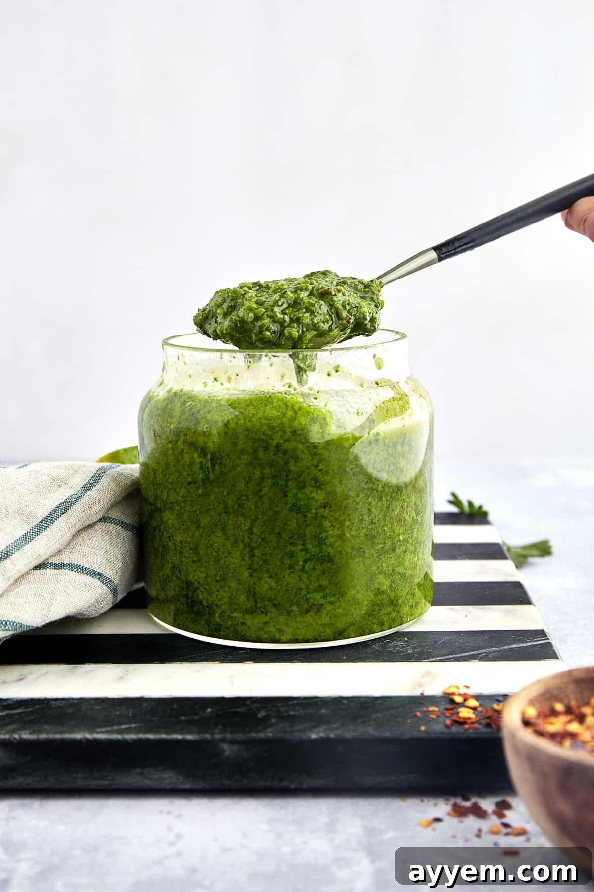 A spoon lifting a scoop of vibrant green Zhoug sauce from a glass jar, ready to be served and enjoyed.