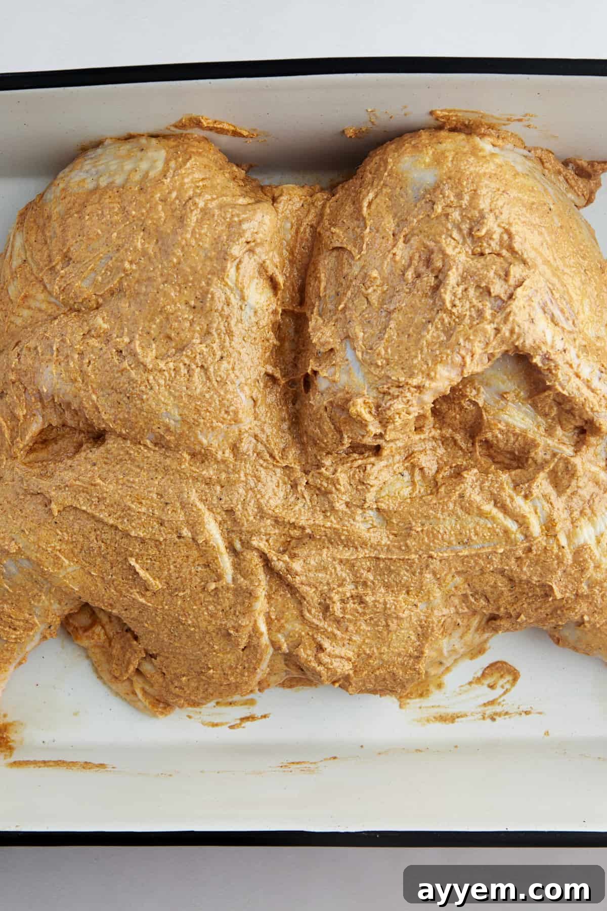 The Art of Roasting a Whole Chicken 9 A raw butterflied chicken covered with a spiced yogurt marinade in a baking dish, ready for roasting.