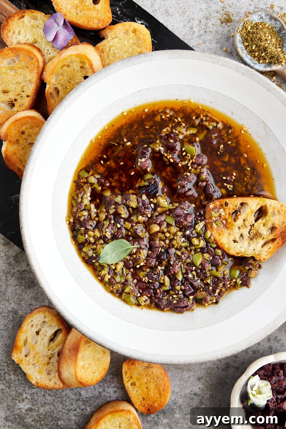 A close-up of a bowl of bread dipping oil, rich with olives, garlic, and za'atar, ready for serving.