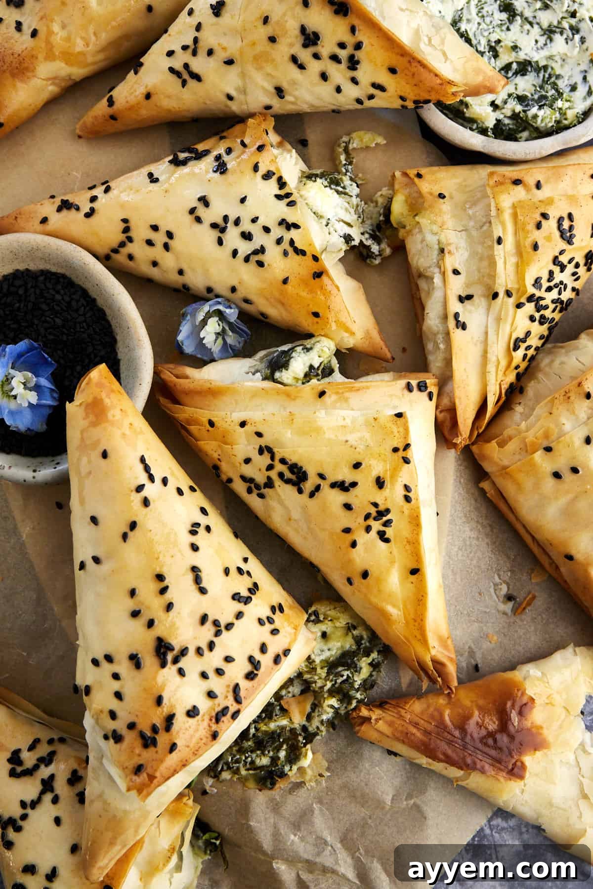Baked spanakopita triangles topped with black sesame seeds on parchment paper.