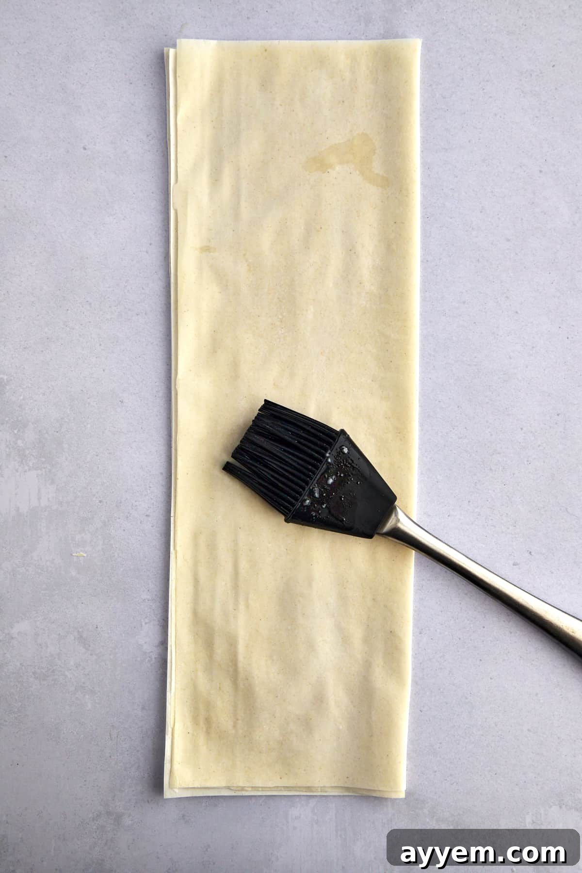 A pastry brush spreading dough over layered phyllo sheets. 