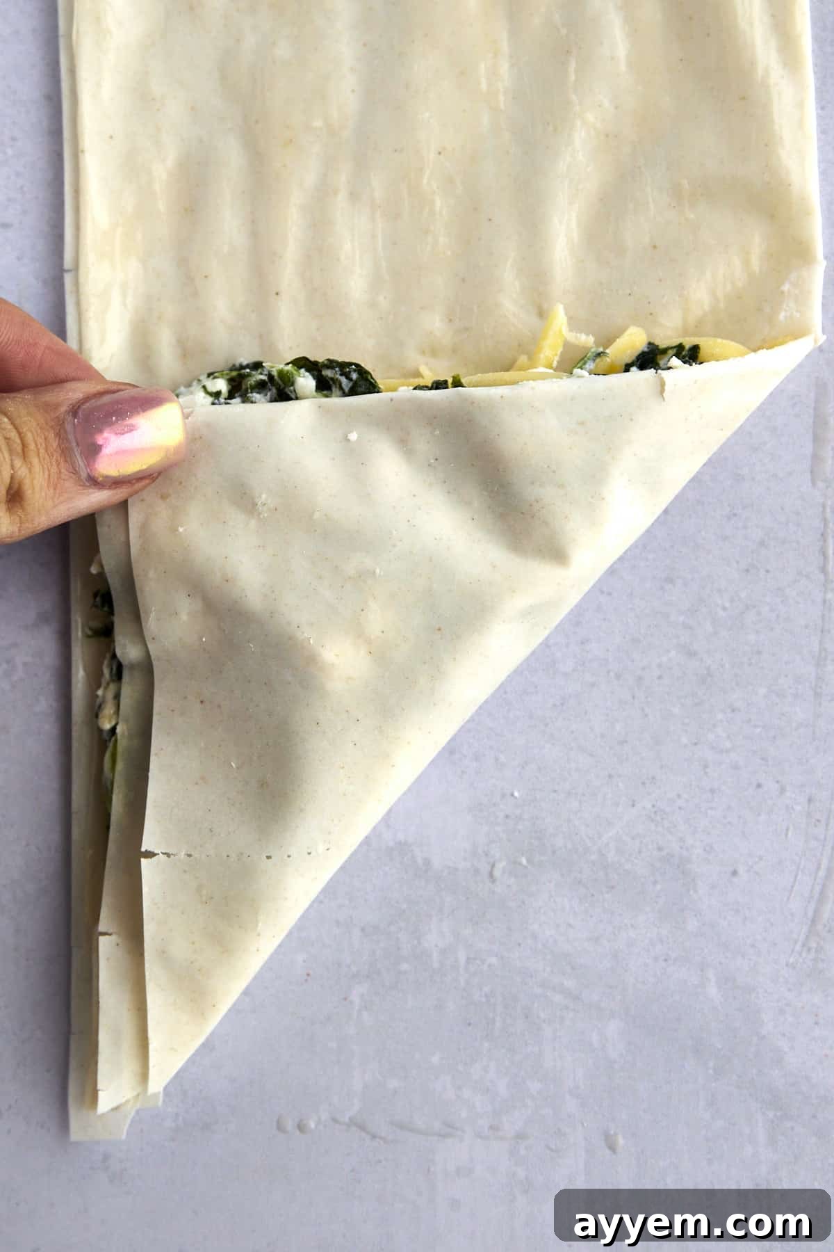A hand folding phyllo dough over spanakopita filling. 