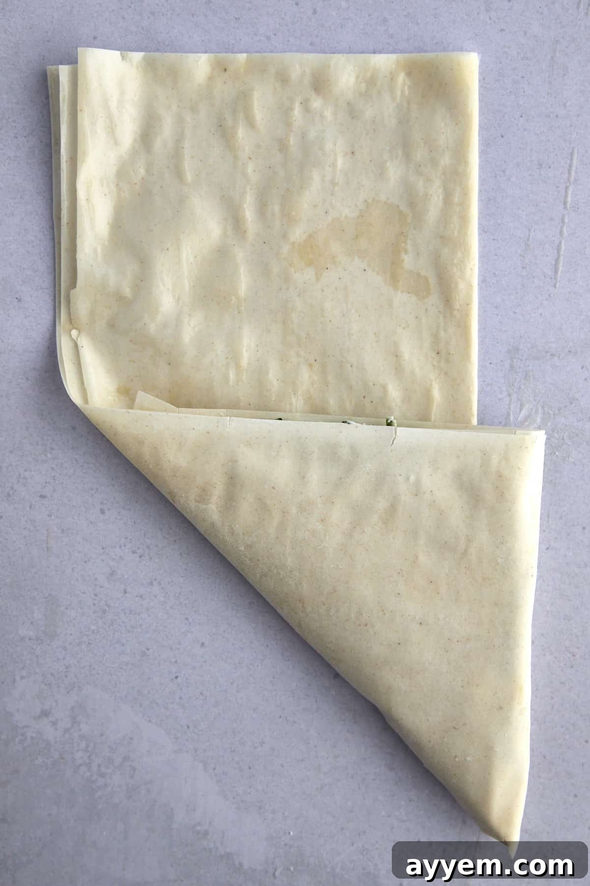 Raw phyllo dough being folded into a triangle. 