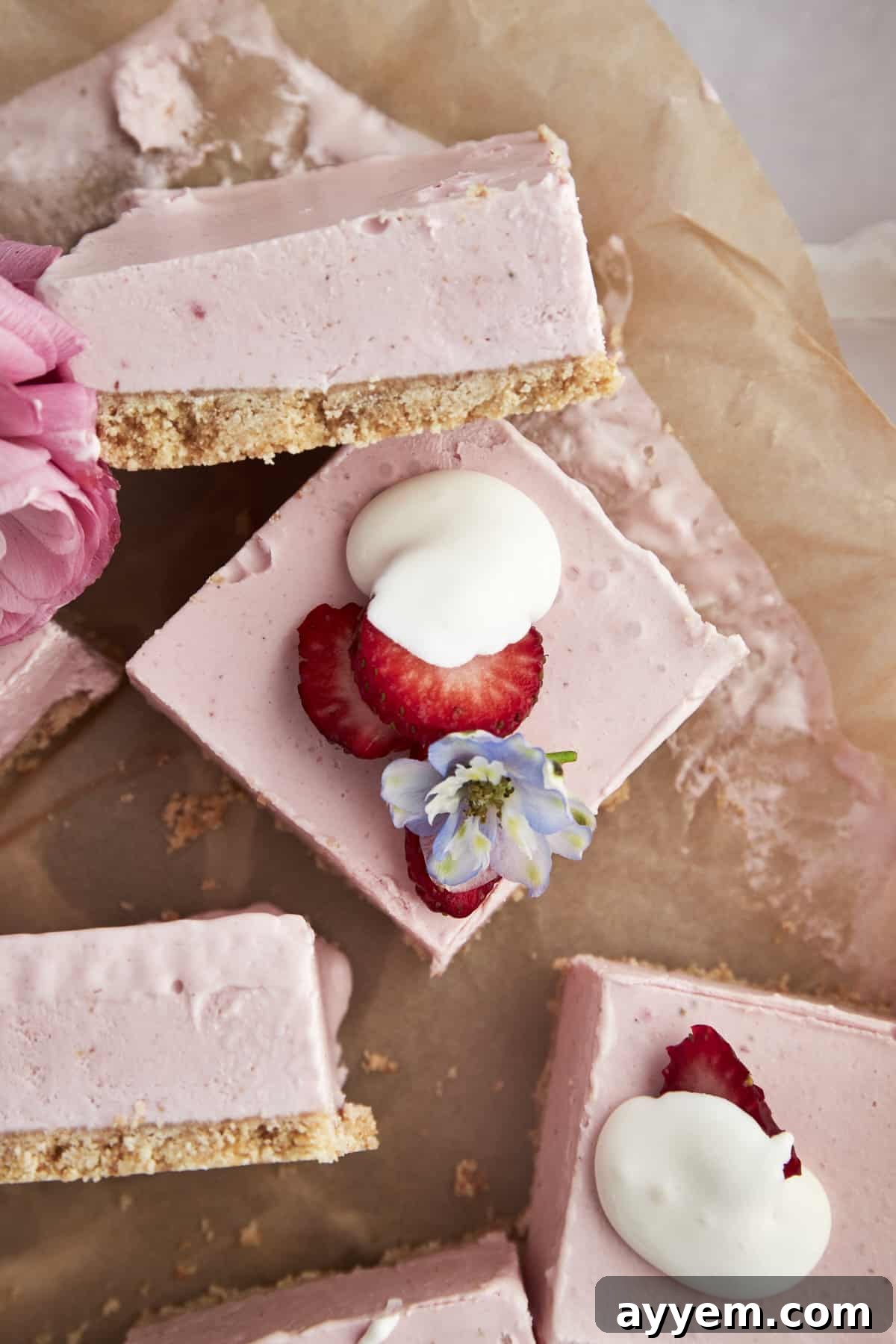 Overhead shot of perfectly cut no-bake strawberry cheesecake squares on parchment paper, ready to be served.
