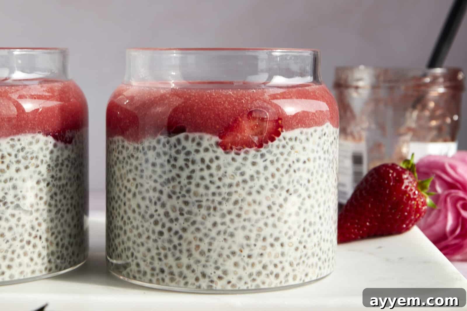 Side view of a jar of strawberry chia pudding topped with strawberry puree and sliced strawberries.