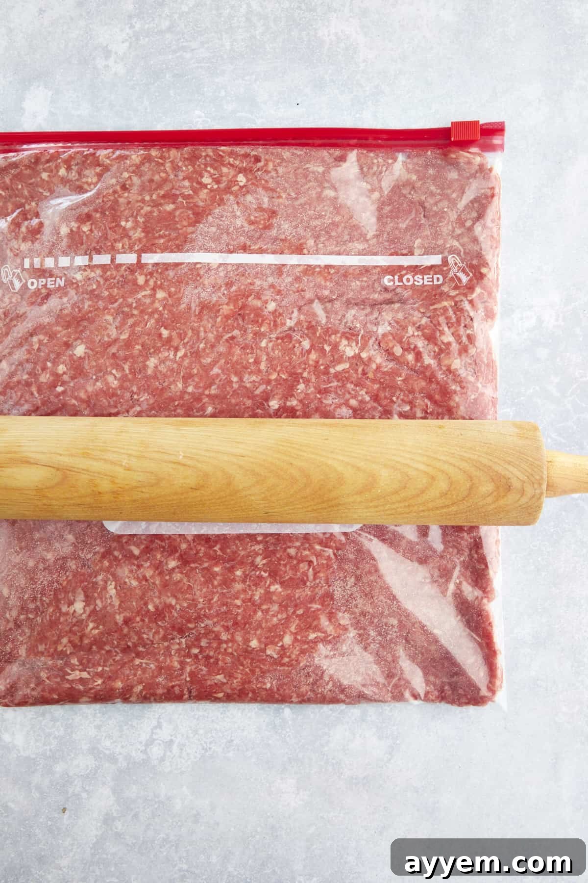A rolling pin flattening raw ground beef in a sealable bag. 