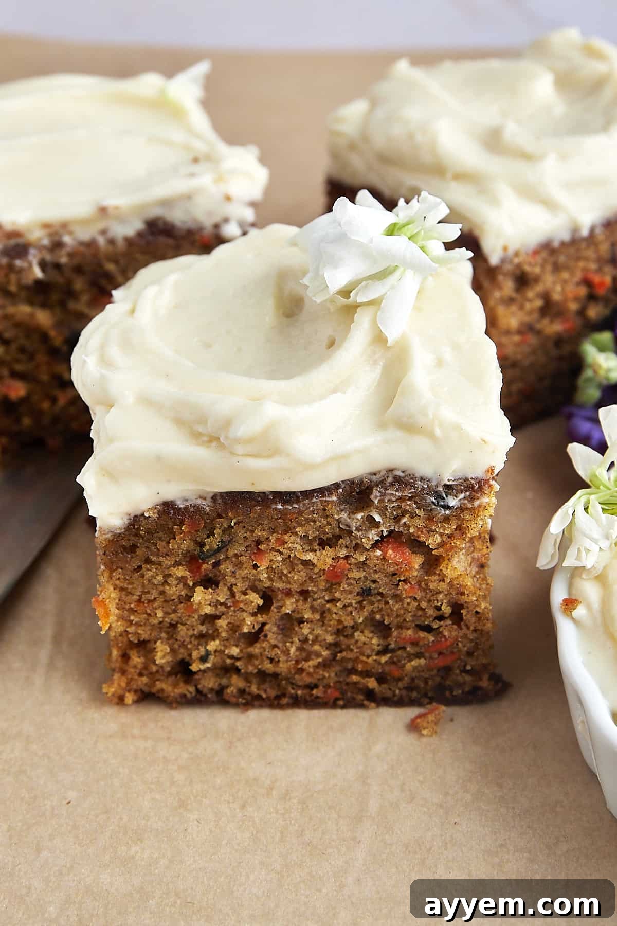 A slice of moist carrot cake with cream cheese frosting, showing shredded carrots and nuts.