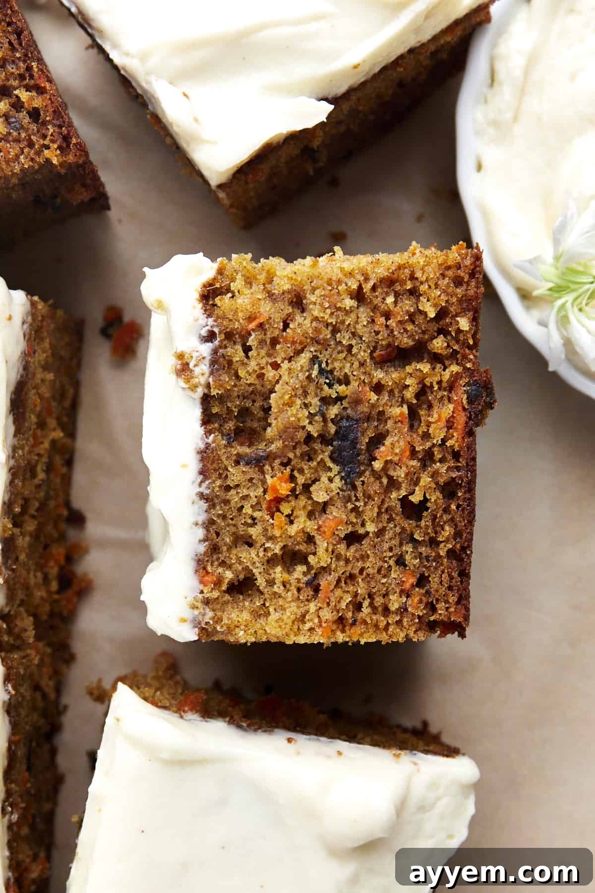 Side view of a slice of carrot cake, showcasing the moist batter, shredded carrots, and nuts, all topped with thick cream cheese frosting.