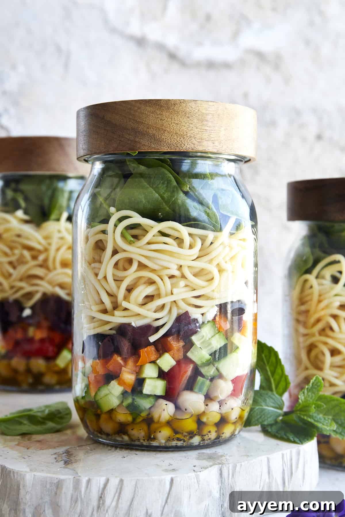 A mason jar salad with olive oil dressing, chopped veggies, spaghetti, and spinach with the lid on top. 