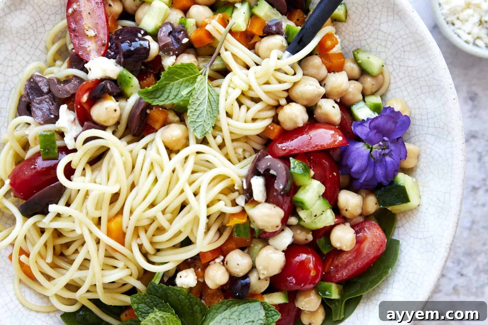 A bowl of spaghetti salad with a fork twirled around the noodles. 