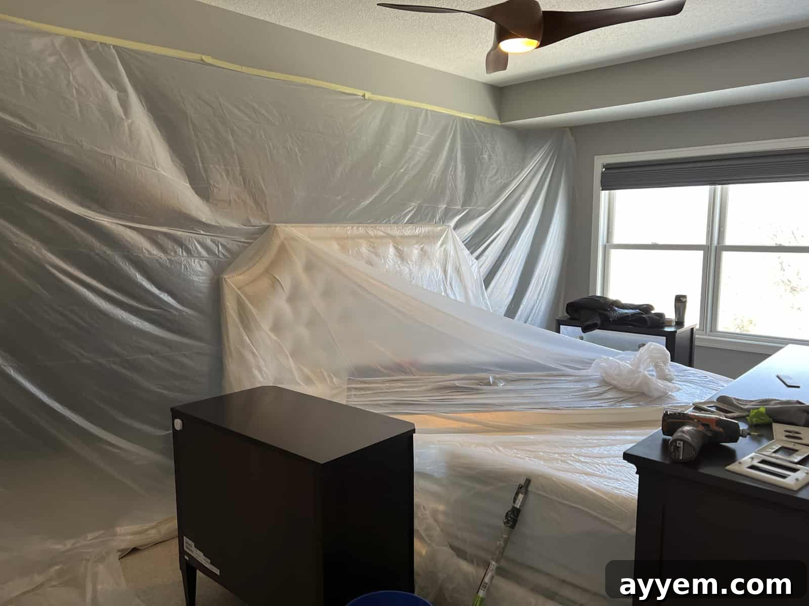 A bedroom meticulously covered with plastic sheeting and drop cloths, prepared for painting.