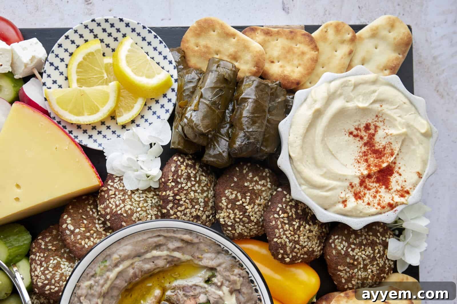 Close up of a section of a mezze platter featuring toum, pita, stuffed grape leaves, falafel, and lemon wedges. 