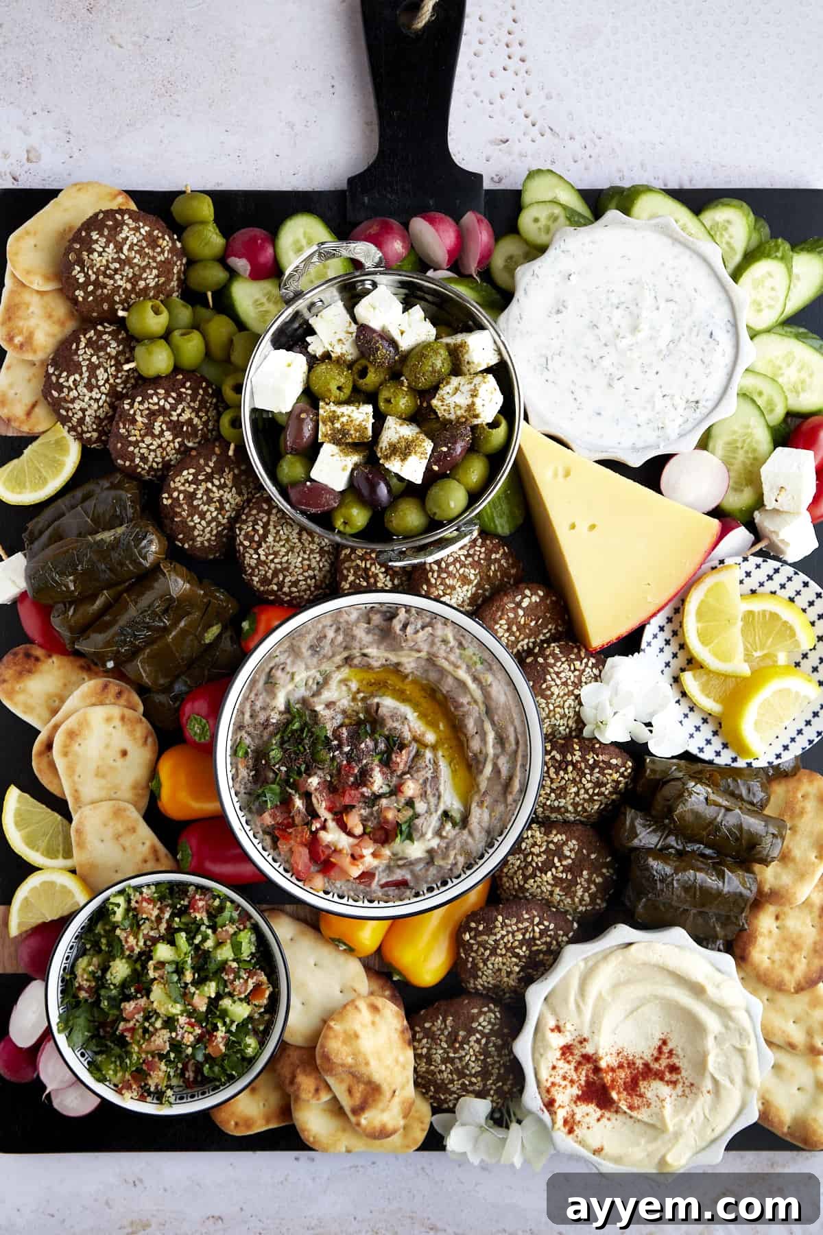 Overhead image of a mezze platter with dips and spreads, cheese, fresh veggies, pita, falafel, and stuffed grape leaves. 