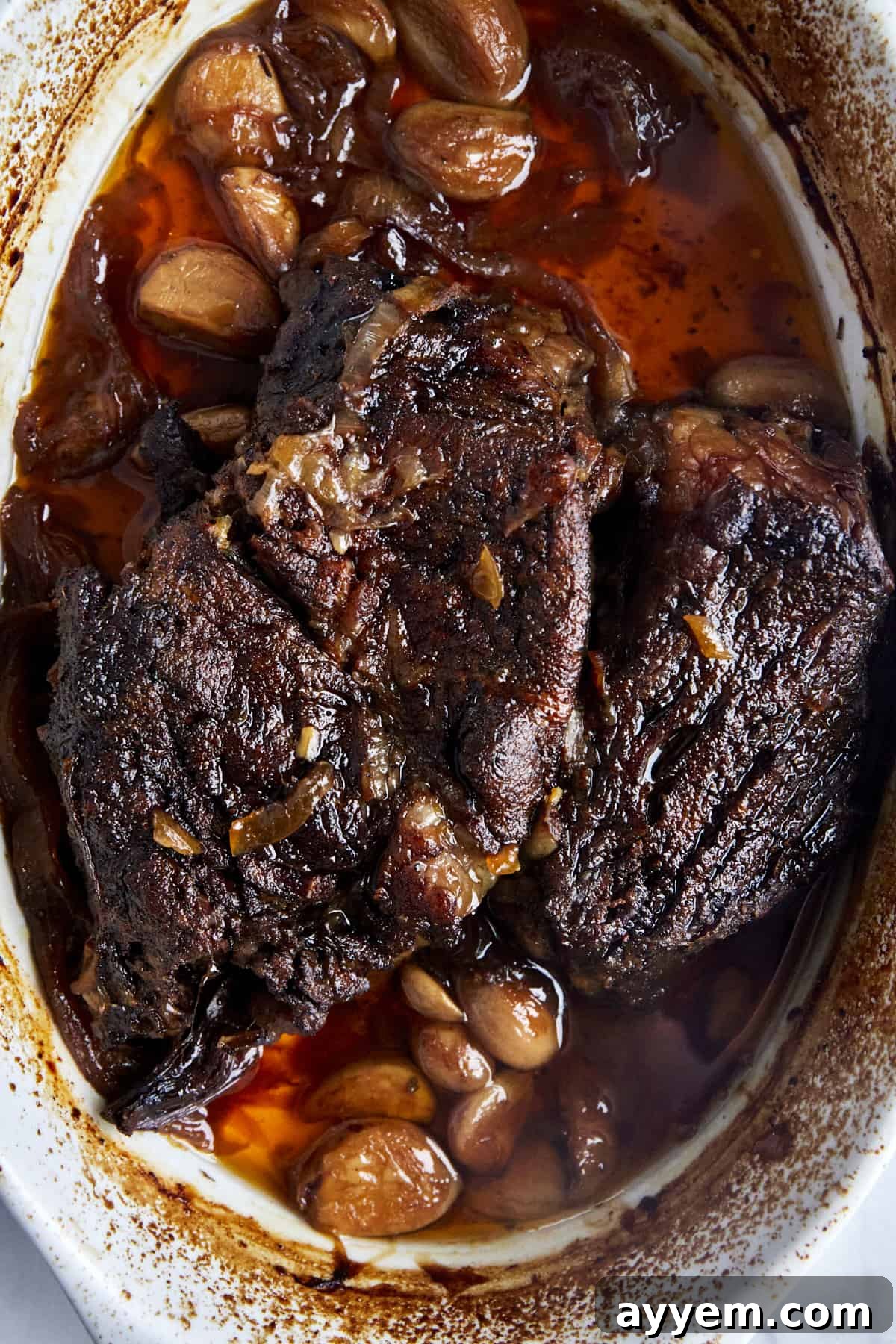 Whole roasted pot roast in a baking dish with onions and garlic. 