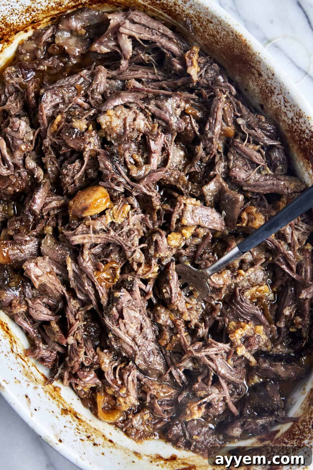 Shredded beef chuck roast in a baking dish with onions and garlic. 