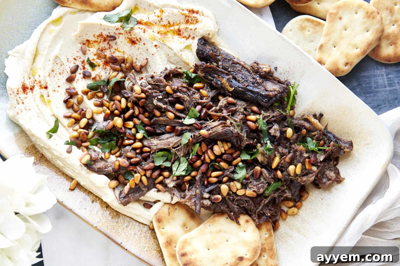 A platter with hummus topped with shredded pot roast meat, toasted pine nuts, and parsley. 