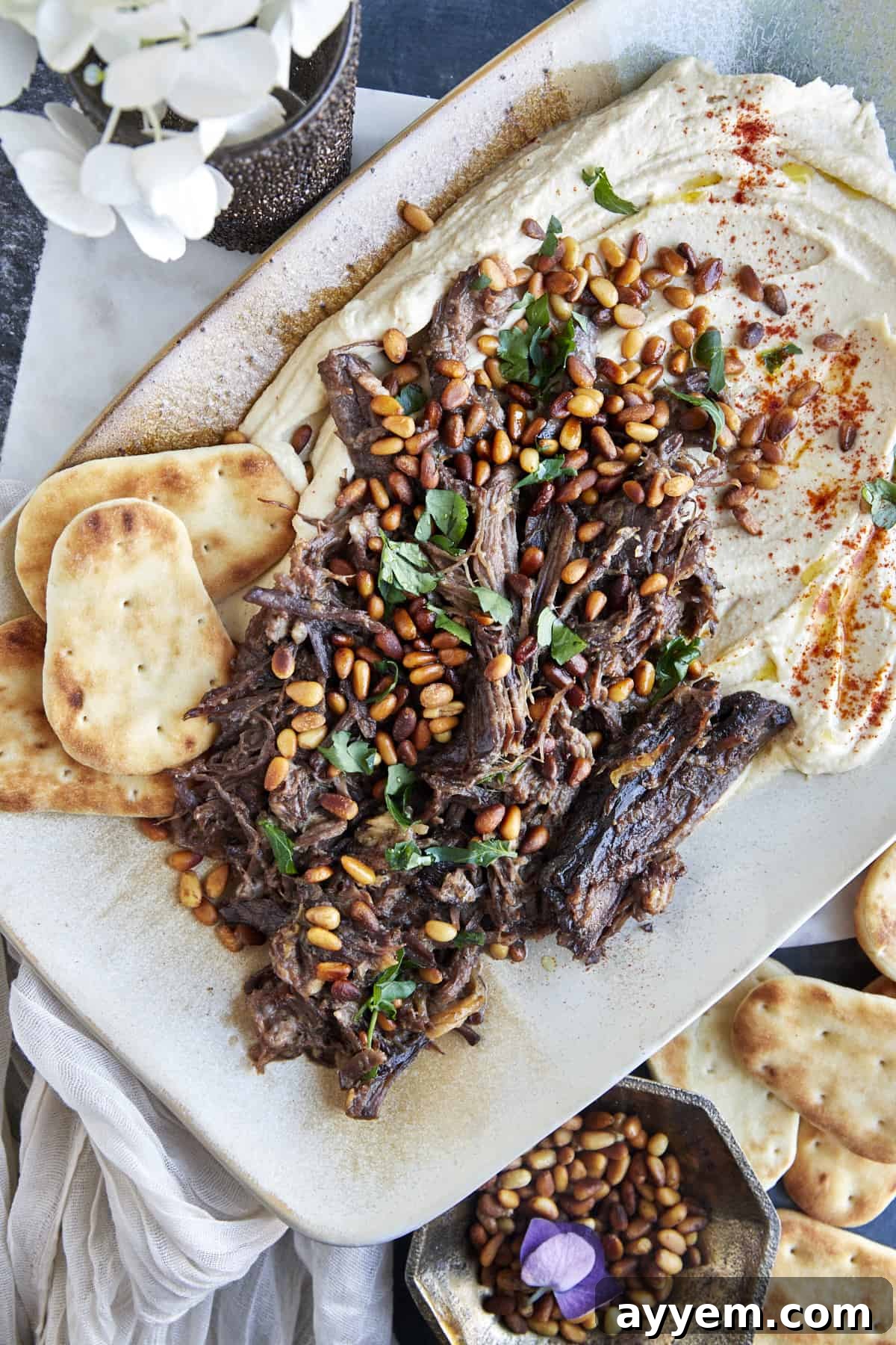 Hummus with meat on a platter with pita chips on the side.