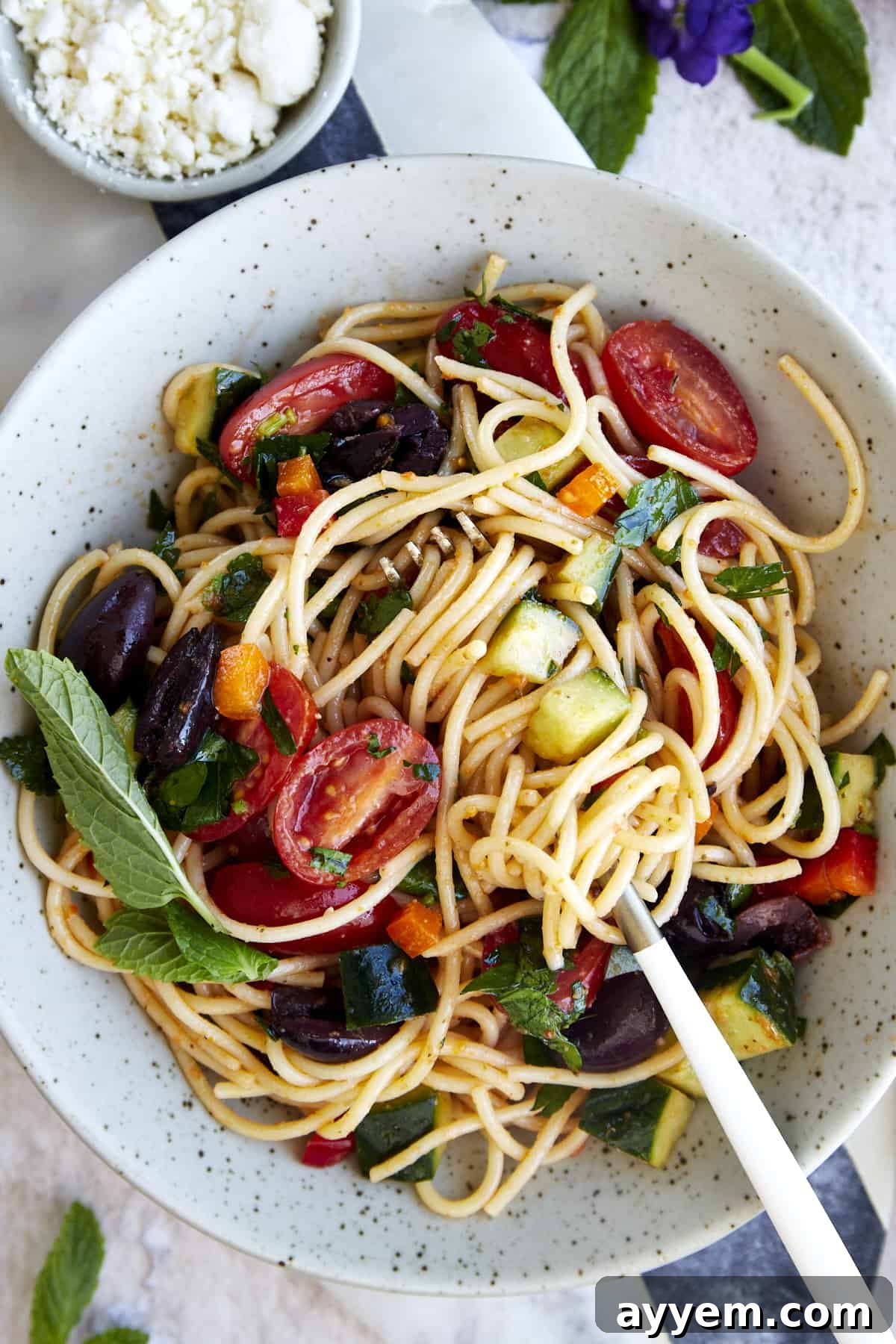 A bowl of vibrant Greek spaghetti pasta salad with noodles twined around a fork, ready to be enjoyed.