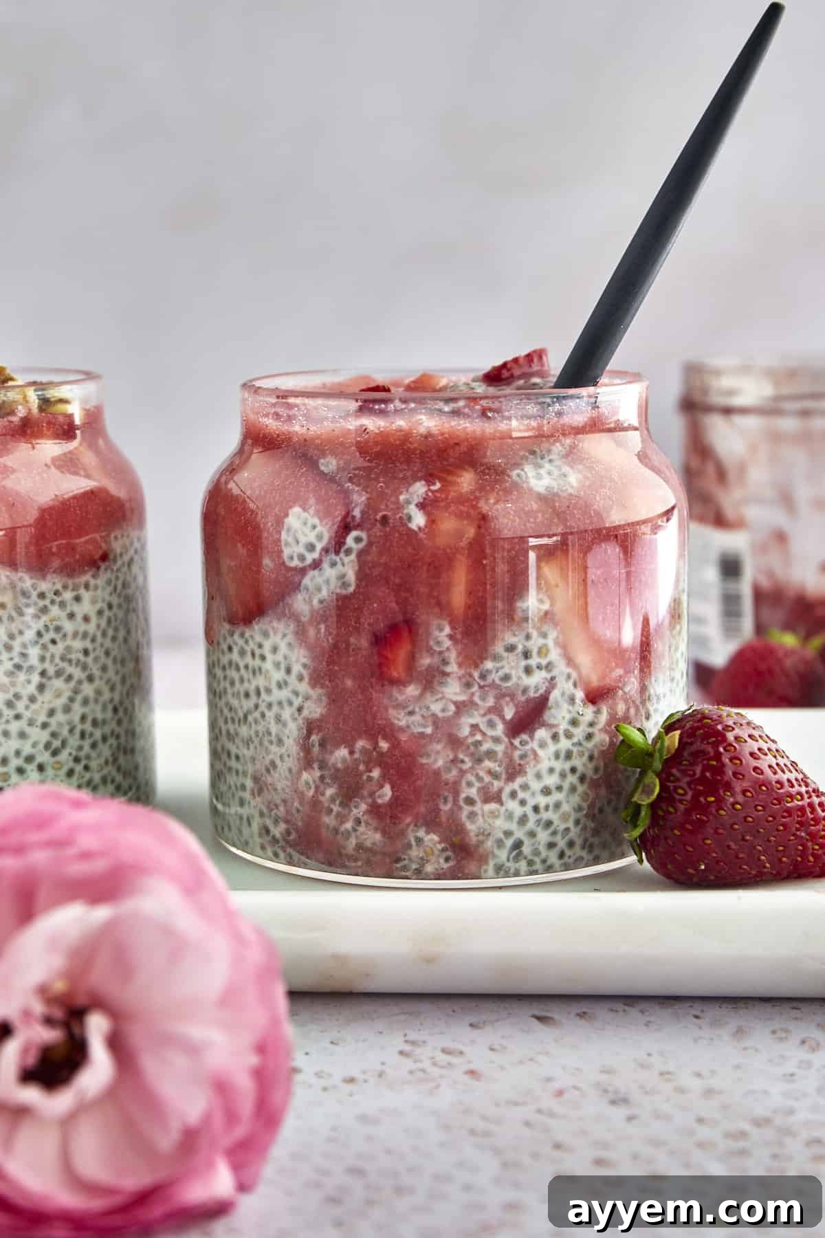 A mason jar filled with vibrant strawberry chia pudding, topped with fresh berries and coconut flakes.