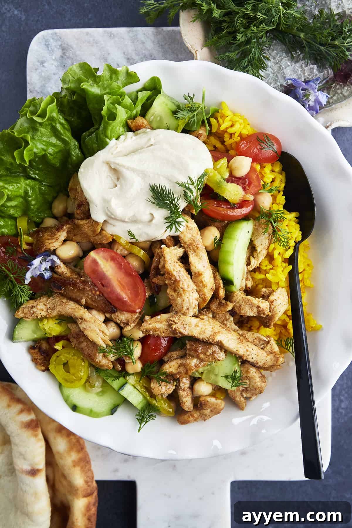 A bowl of delicious chicken shawarma with fluffy rice, fresh veggies, and a dollop of creamy hummus.
