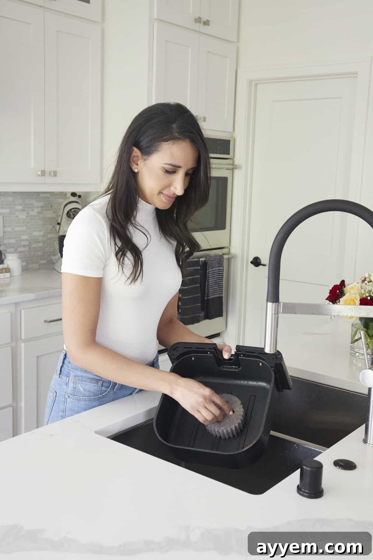 A woman using a sponge to clean the basket of an air fryer in a sink.