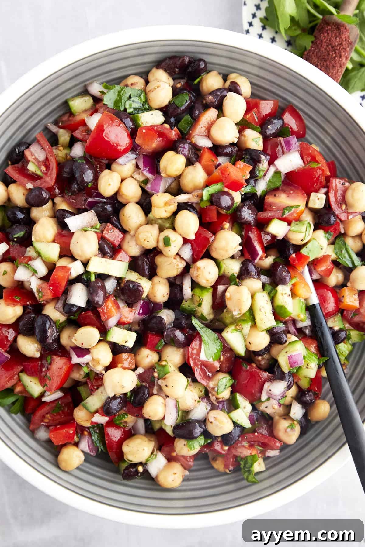 A bowl of balela salad with chickpeas, black beans, fresh veggies, and herbs, ready to be served.