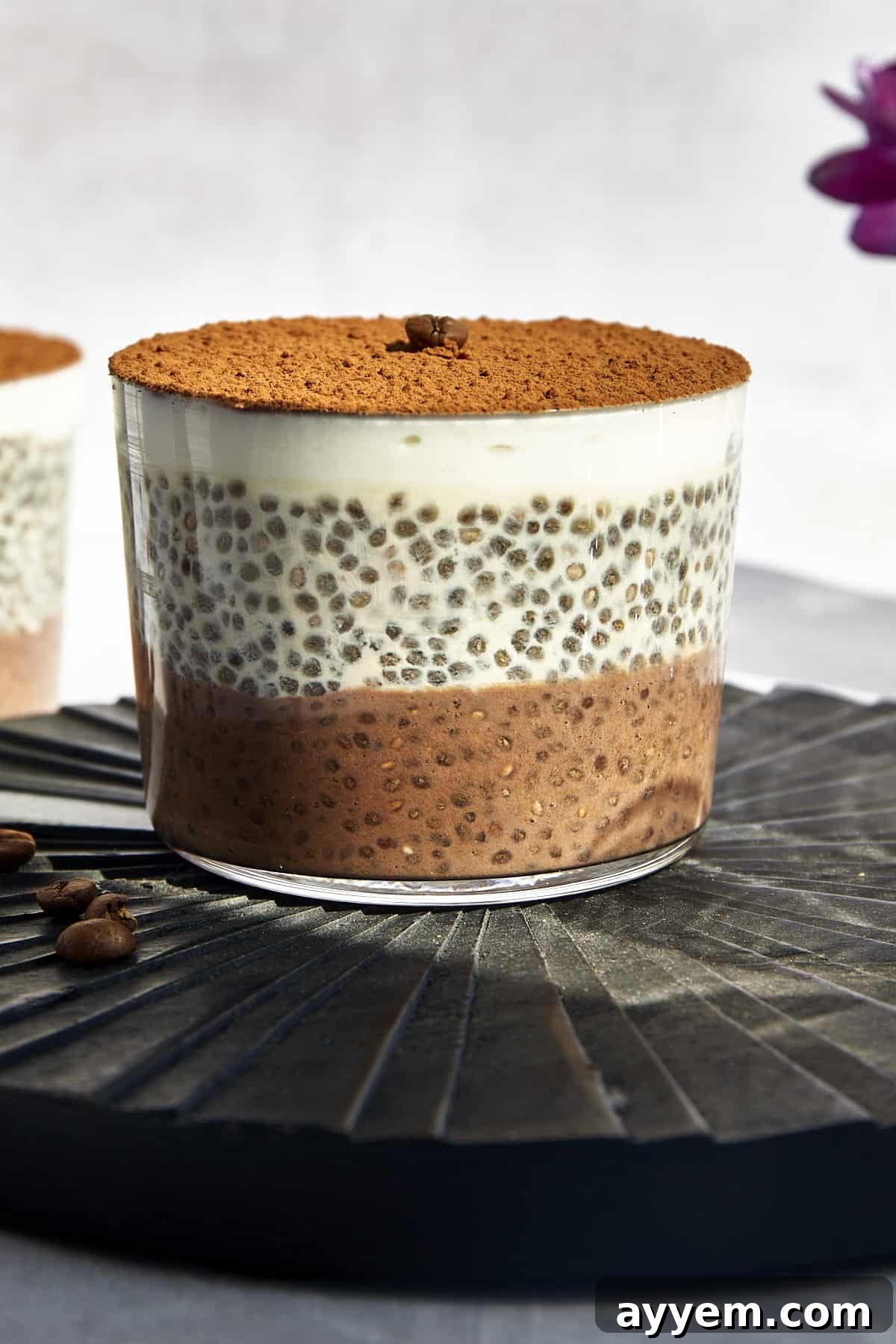 A jar of layered tiramisu chia pudding with a coffee layer, vanilla layer, yogurt layer, and cocoa powder on top.