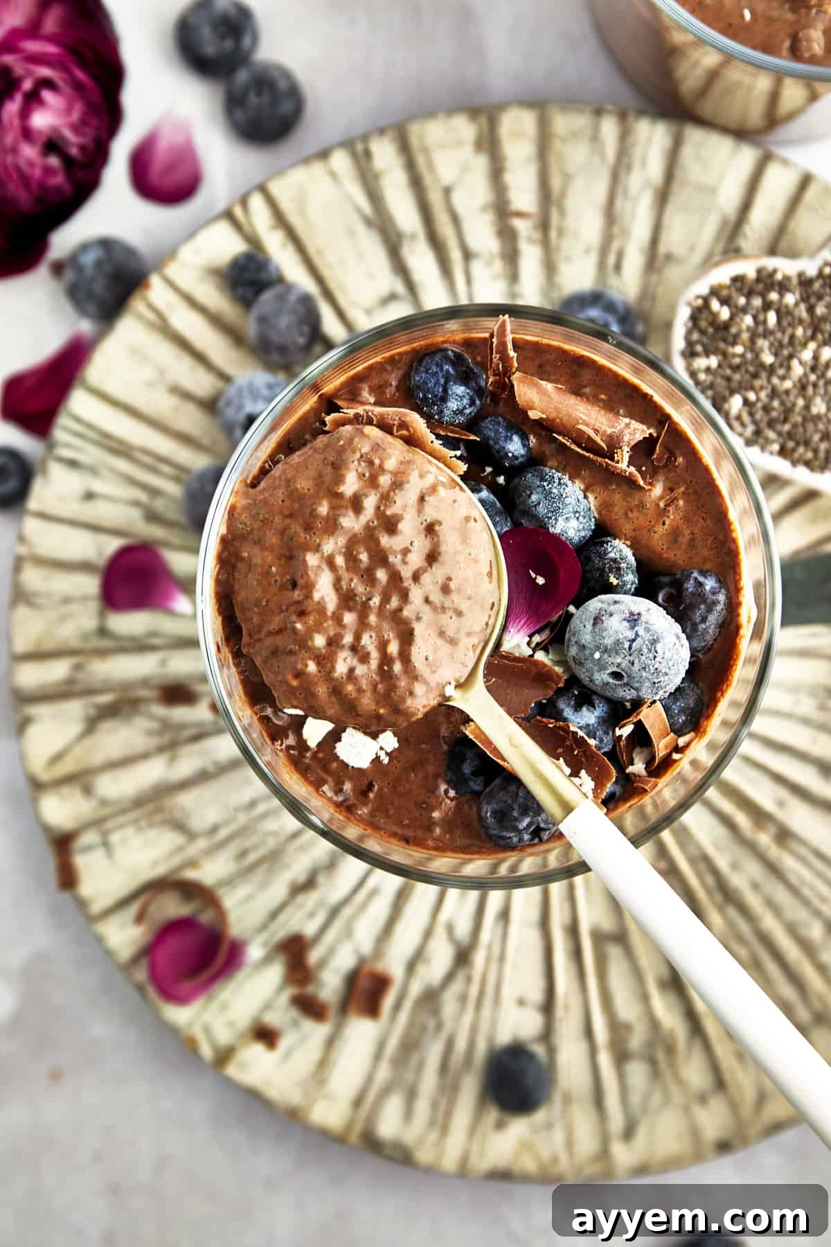 A glass jar of chocolate chia pudding with a spoon inside, garnished with fresh berries and a hint of mint, suggesting readiness for consumption.
