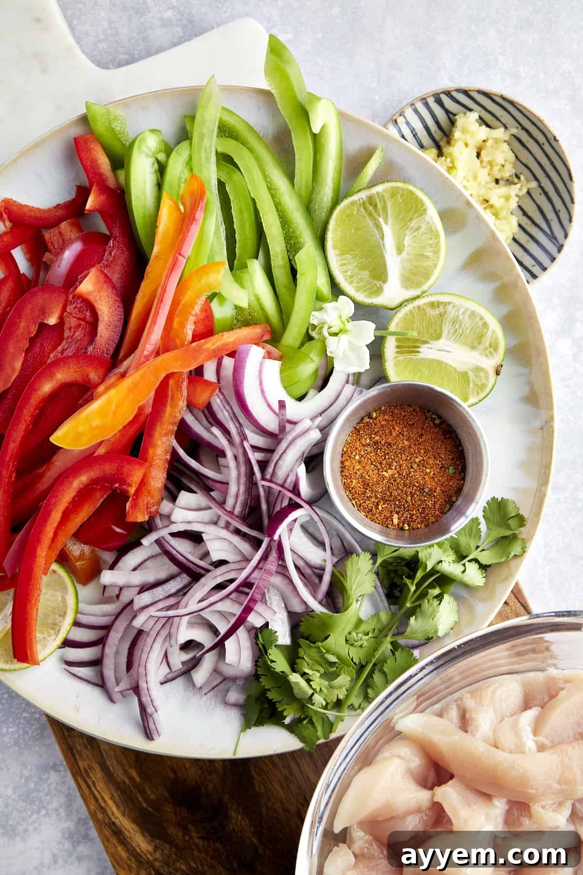Air fryer chicken fajita ingredients including sliced red and green peppers, red onion, lime halves, taco seasoning, cilantro, and chicken. 