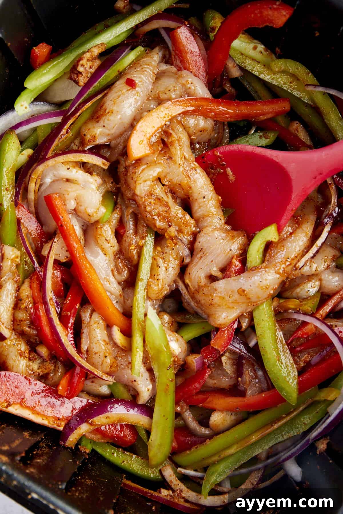 Raw chicken, peppers, and red onions coated with taco seasoning in an air fryer. 