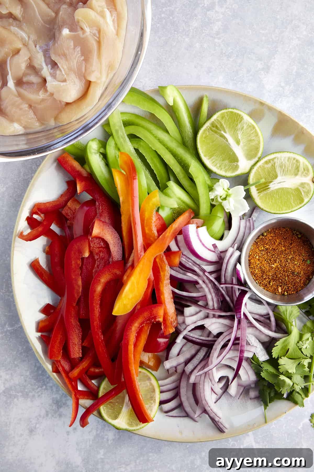 Sliced chicken, red and green bell peppers, red onion, a halved lime, cilantro, and fajita seasonings. 