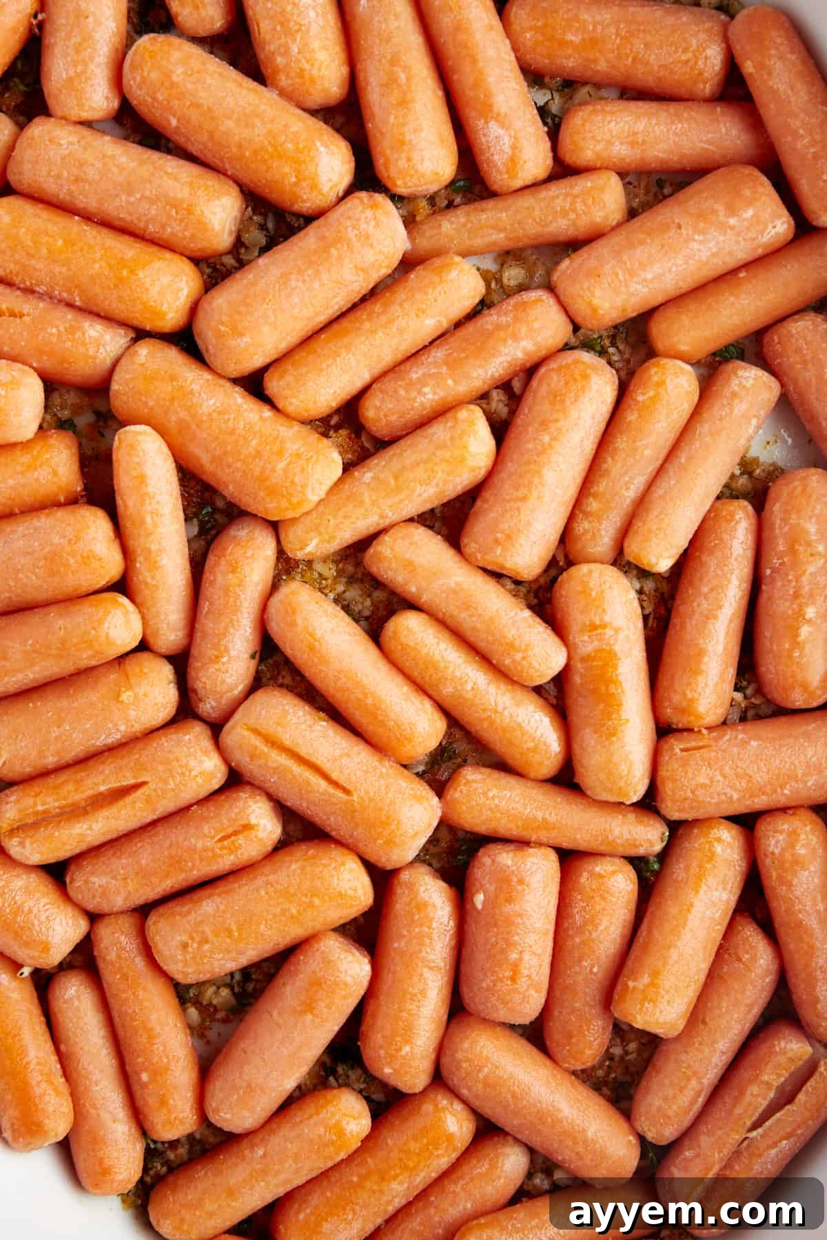 Raw baby carrots in a baking dish on top of a butter, panko, Parmesan coating. 