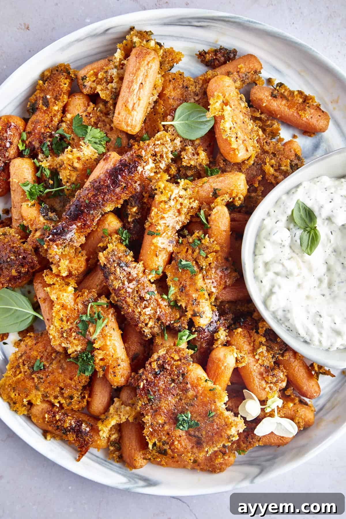 A serving platter full of Parmesan oven roasted carrots with a bowl of tzatziki on the side. 