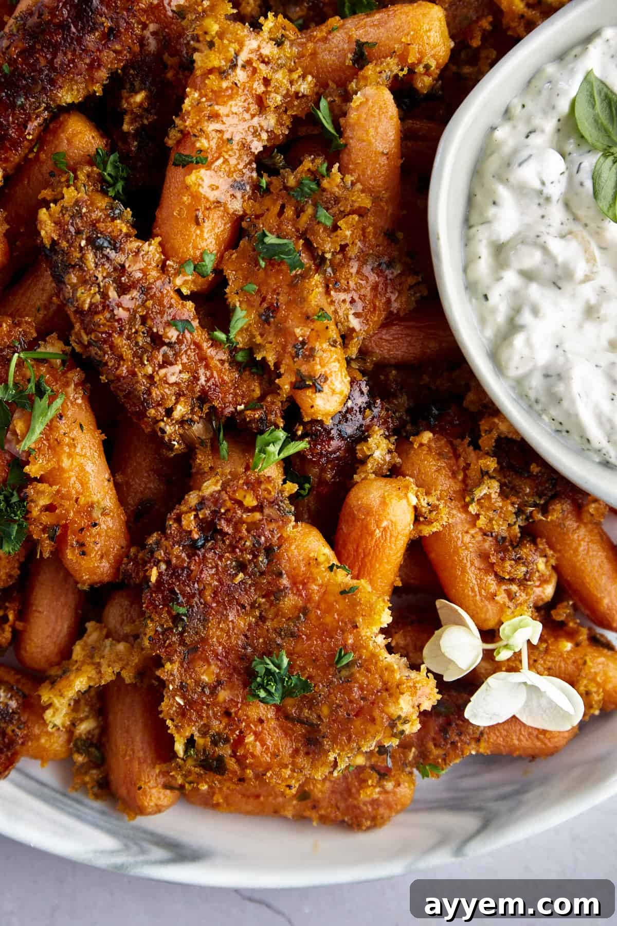 Close up image of Parmesan oven roasted carrots with a bowl of tzatziki on the side.