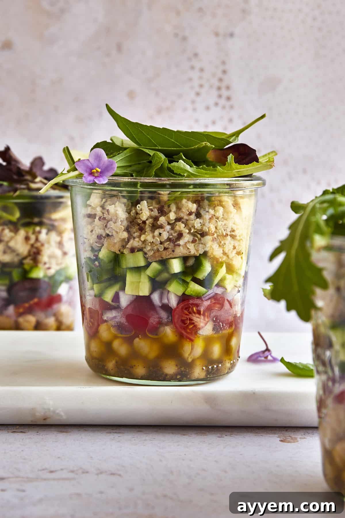A beautifully layered Mediterranean Quinoa Salad in a Jar, featuring olive oil dressing, chickpeas, sliced grape tomatoes, chopped red onion, diced cucumbers, cooked chicken, fluffy quinoa, and fresh greens.
