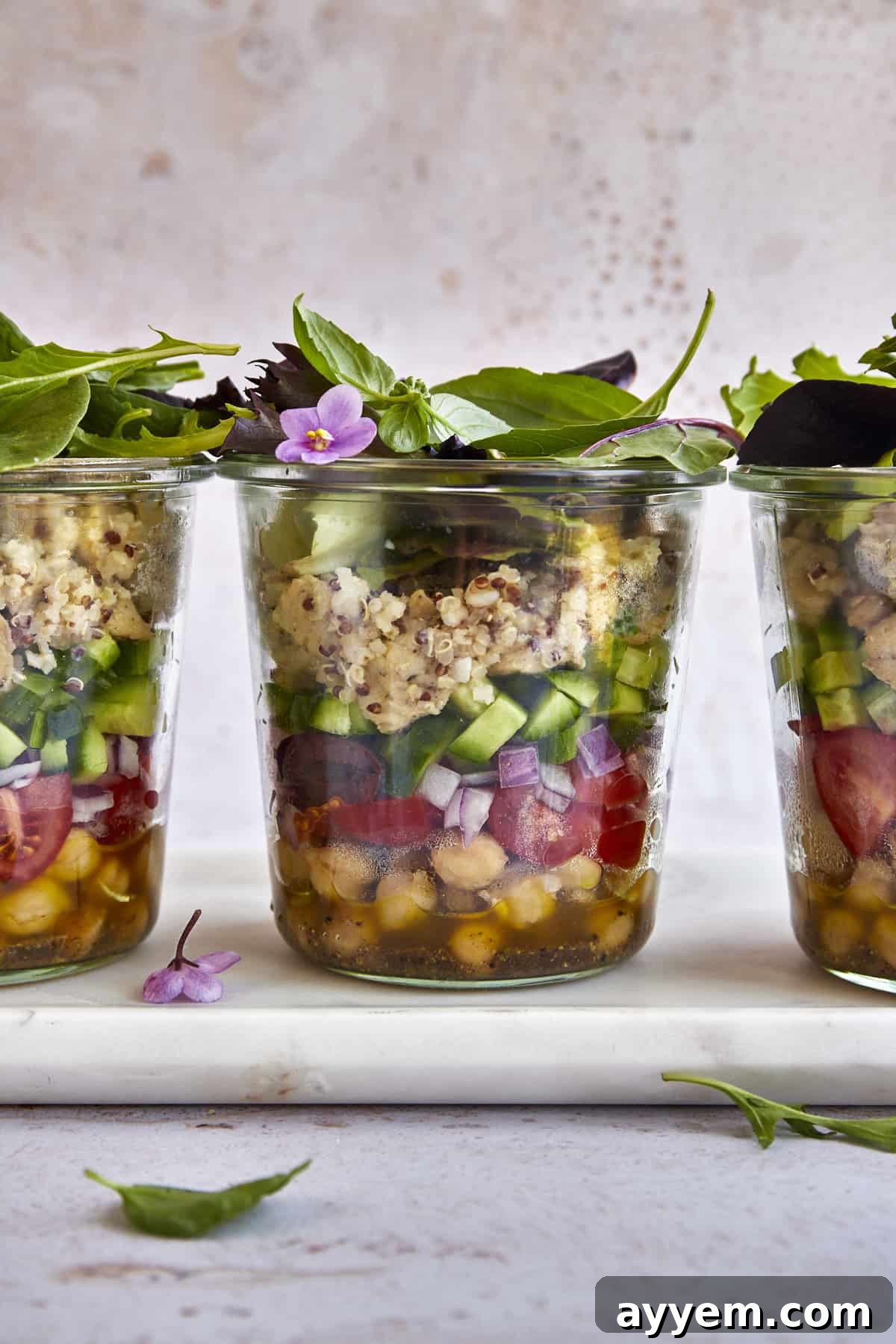 Three Mediterranean quinoa salad in a jar portions lined up, showcasing the vibrant layers of ingredients before mixing.