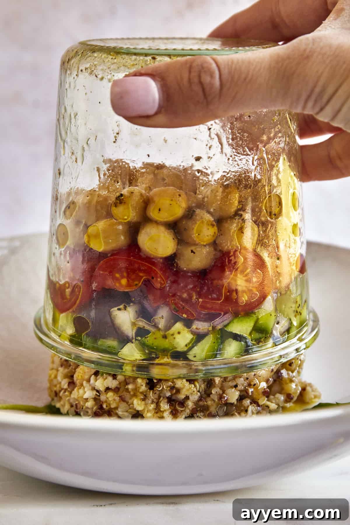 A Mediterranean quinoa salad in a jar being inverted into a bowl, showing the beautiful layers falling into place for mixing.