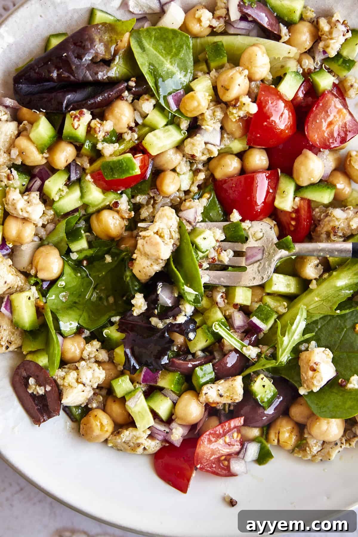 Overhead image of a Mediterranean quinoa salad, previously in a jar, now dumped into a bowl and ready to be mixed. It shows greens, veggies, quinoa, chicken, and chickpeas.