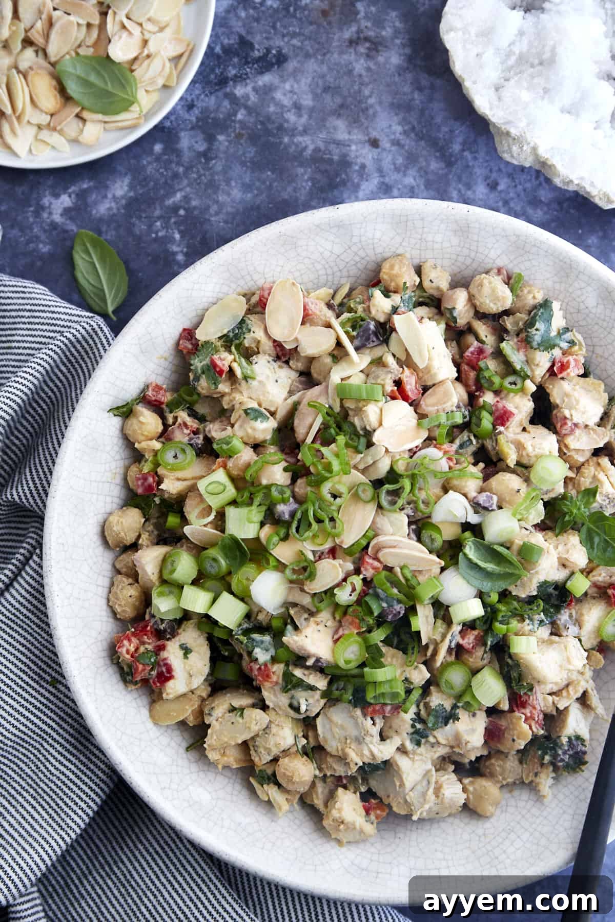 An overhead view of a large, inviting bowl of Chickpea Chicken Salad, generously garnished with toasted slivered almonds and bright green onions, highlighting its vibrant colors and appealing textures.
