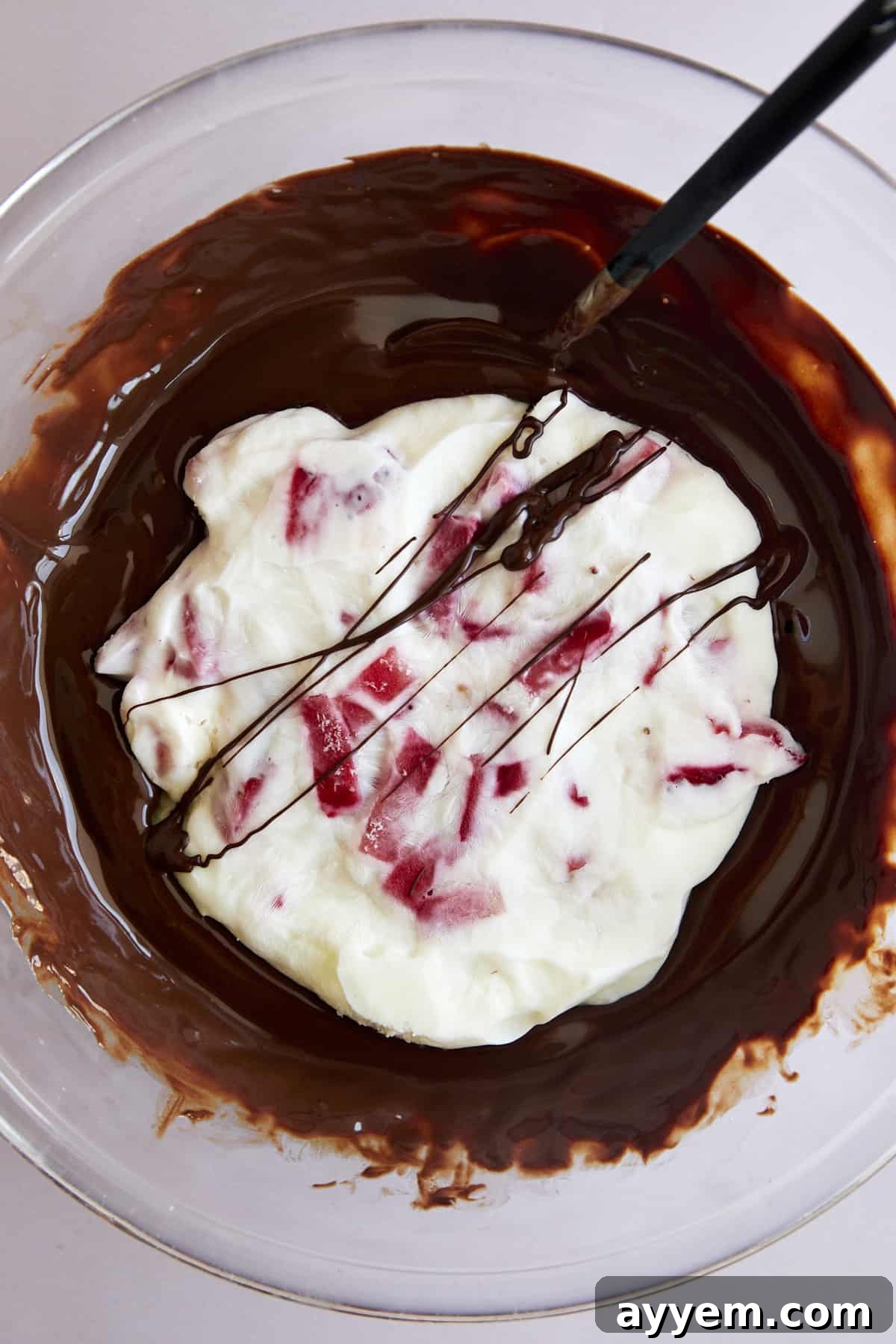 An overhead shot of a strawberry yogurt cluster being dipped into a bowl of smooth, melted chocolate.