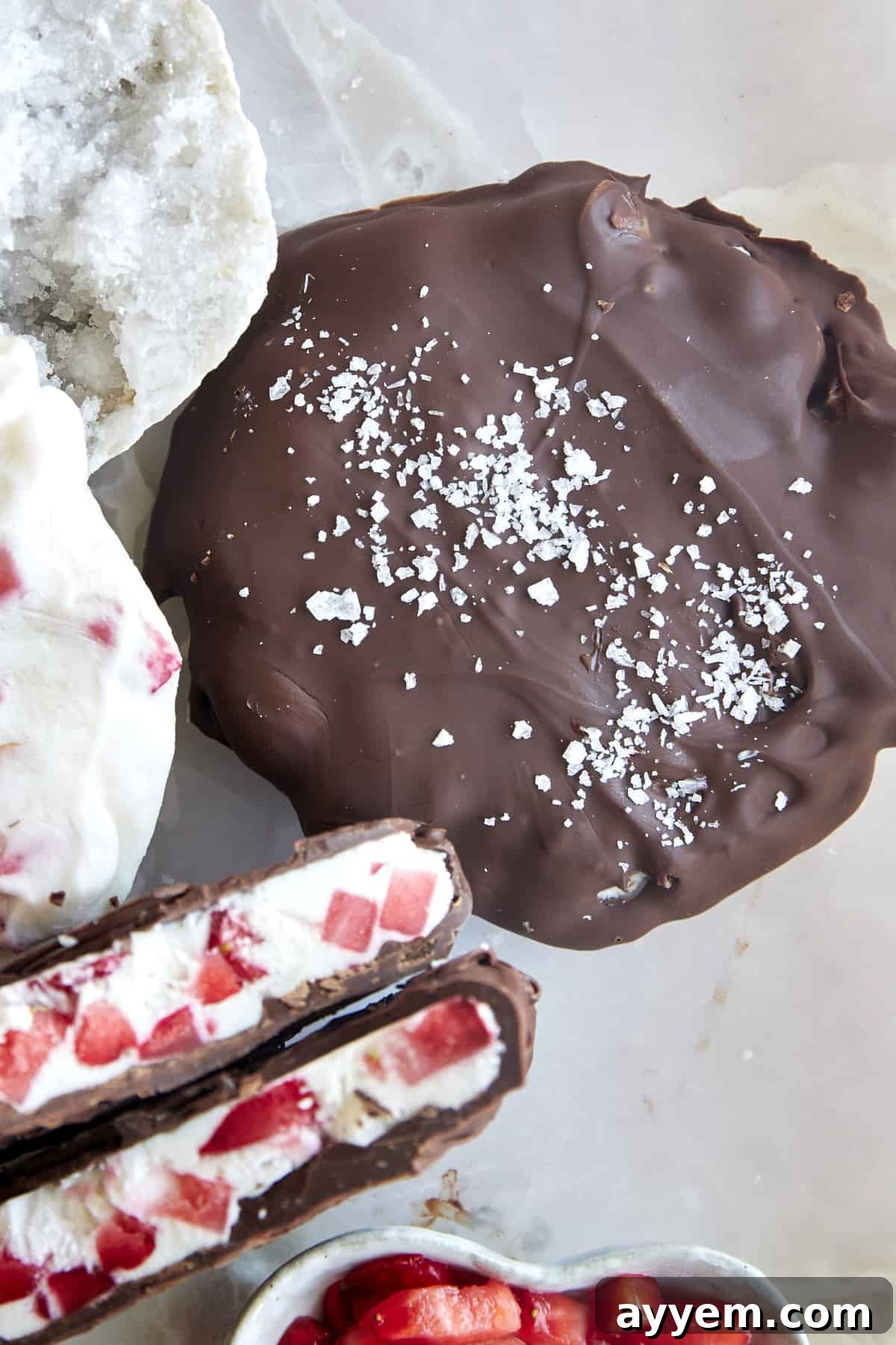 Two perfectly prepared chocolate strawberry yogurt clusters, one whole and one split to show its creamy interior, lightly sprinkled with sea salt.
