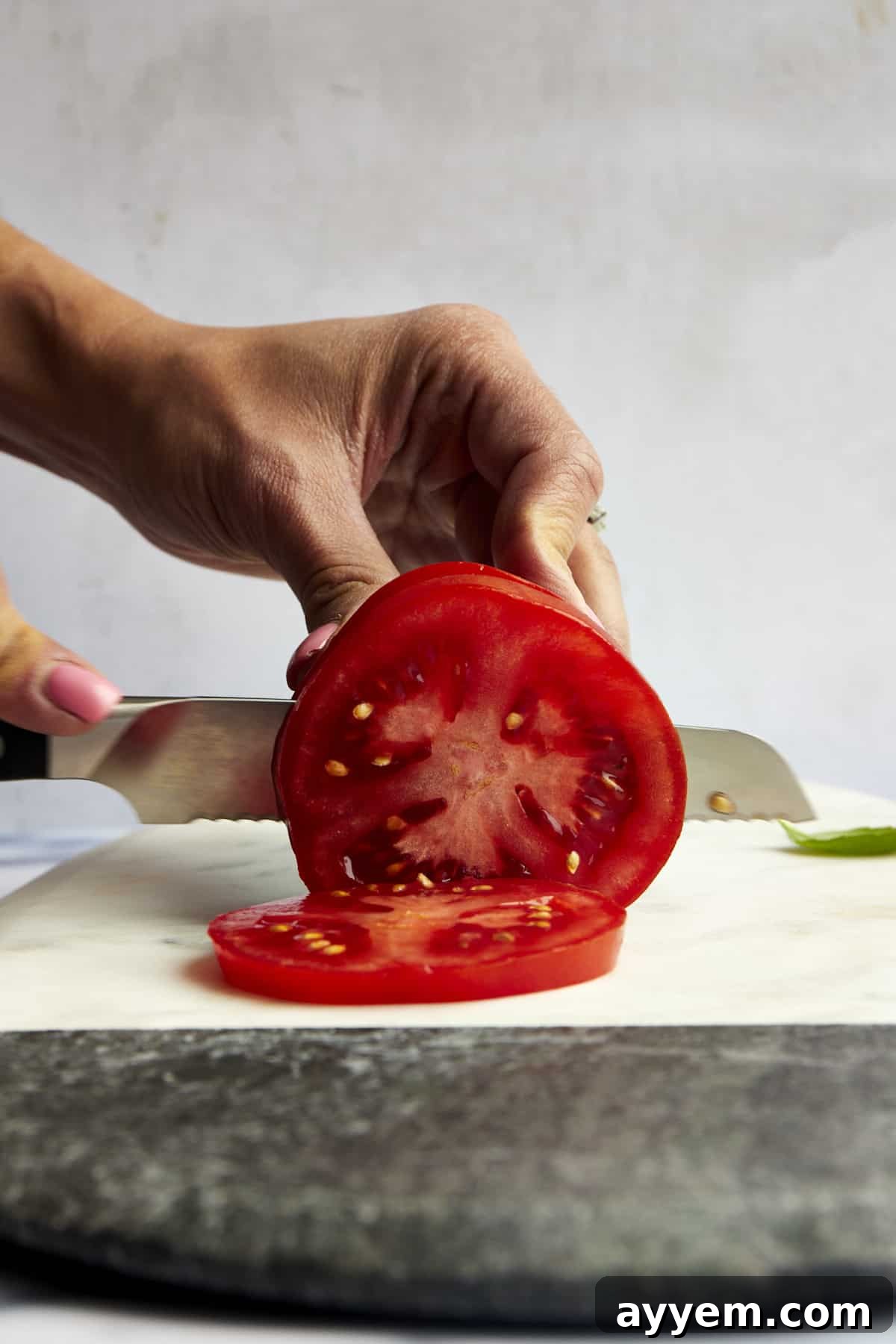 Mastering Tomato Slices Three Essential Techniques 4 A ripe red tomato being carefully cut into thin, uniform slices on a wooden cutting board.