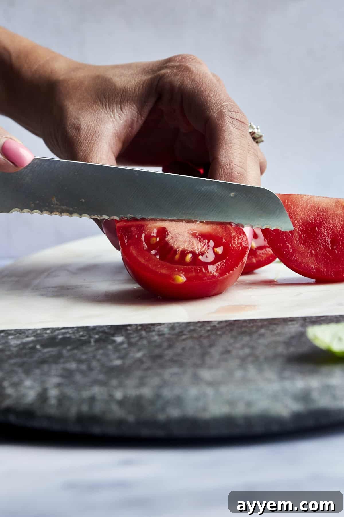Mastering Tomato Slices Three Essential Techniques 6 A red tomato being quartered on a wooden cutting board, with a knife positioned for the final cut.